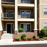 **

"A visually appealing apartment building exterior in a sunny, safe neighborhood. Families and individuals are happily entering and exiting. Emphasize cleanliness, well-maintained landscaping, and security features (like visible security cameras)."

**